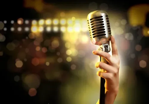 Hand holds a vintage silver microphone, blurred golden bokeh background.