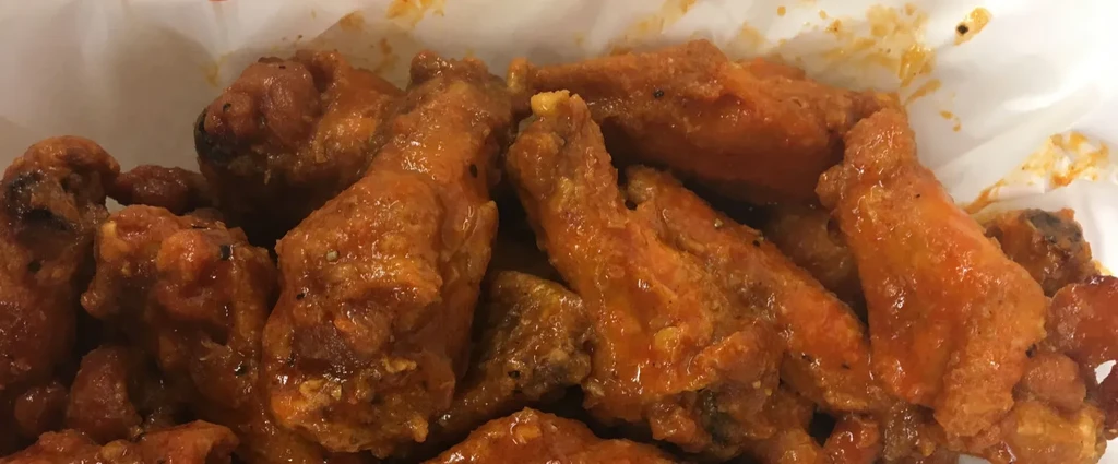 Pile of buffalo chicken wings coated in glistening orange-red sauce.