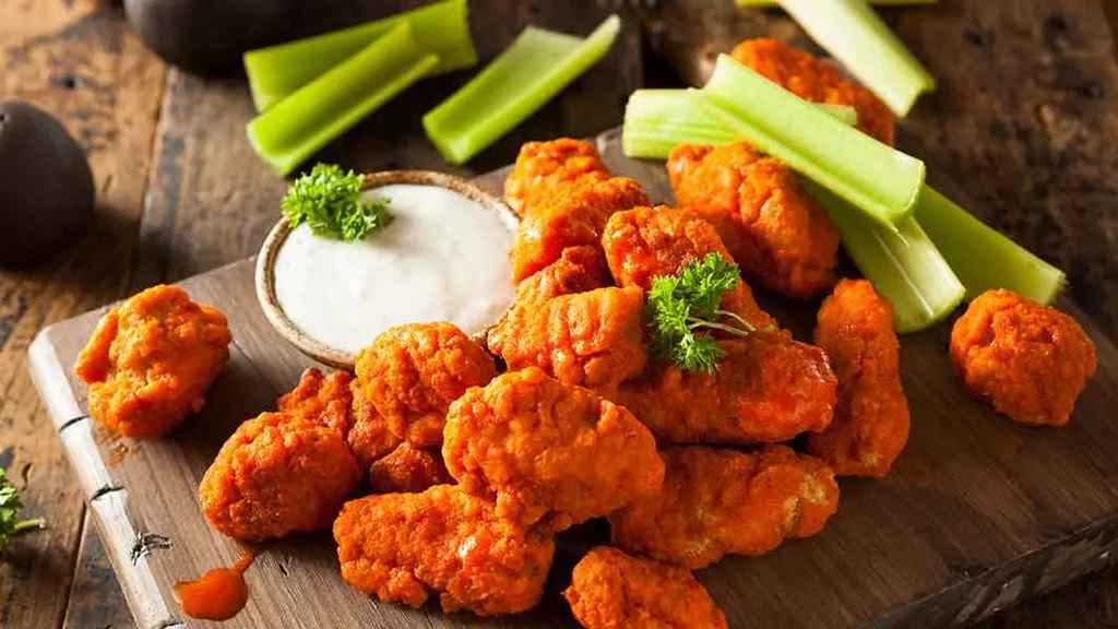 Crispy boneless buffalo wings, celery, and creamy dip on a platter.