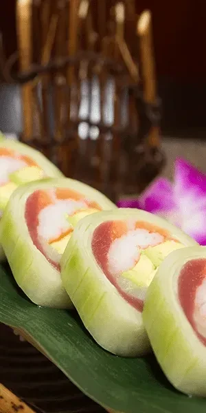 Cucumber-wrapped sushi rolls with colorful fillings on a green leaf.