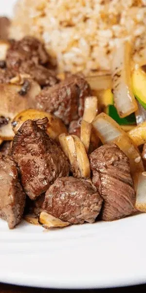 Plate of seared beef cubes, mushrooms, onions, zucchini, and fried rice.