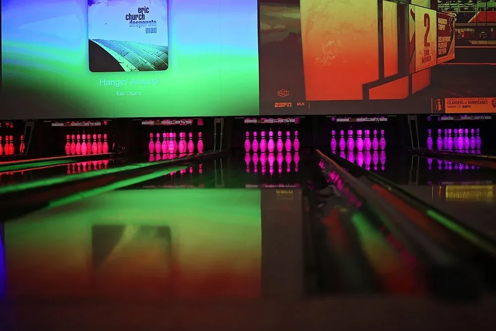 Neon-lit bowling alley with four lanes, glowing pins, and projection screens.