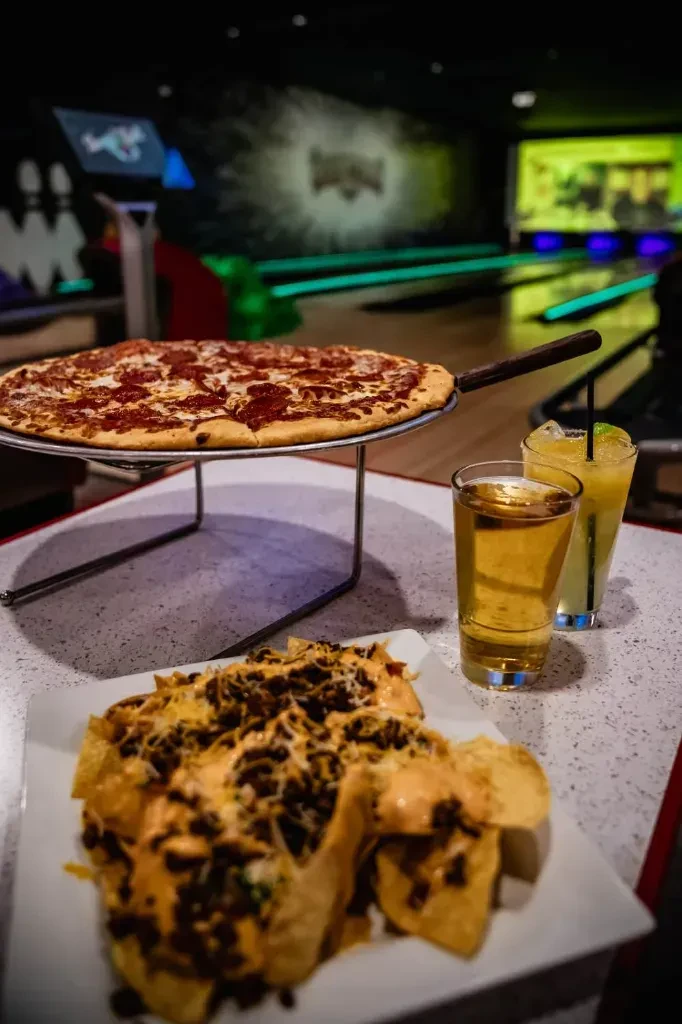 Pepperoni pizza, nachos, and drinks on a table at a bowling alley.