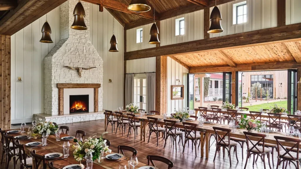Rustic-chic dining hall set for event, with fireplace and outdoor view.