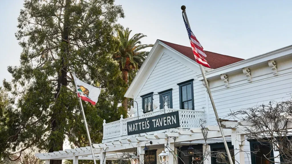Matteis Tavern: White two-story building with red roof, flags, trees.