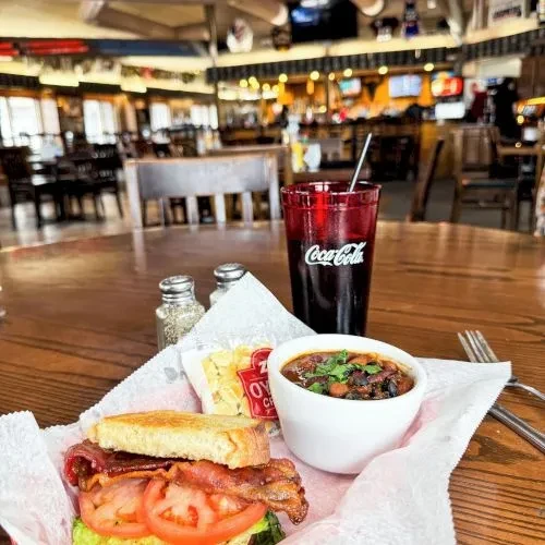 Restaurant meal with sandwich, chili, and Coca-Cola on a wooden table.