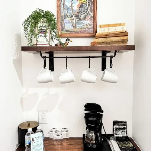 Cozy coffee station with hanging mugs, coffee maker, and bottled water.