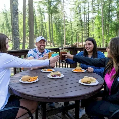 Four smiling people toasting with drinks and food on a deck.