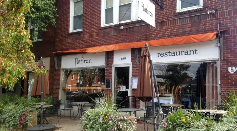 Exterior of Flatiron restaurant with orange awning, outdoor patio, and greenery.