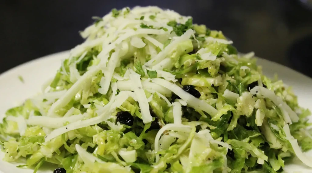 Close-up of shredded green salad with cheese, raisins, and herbs.