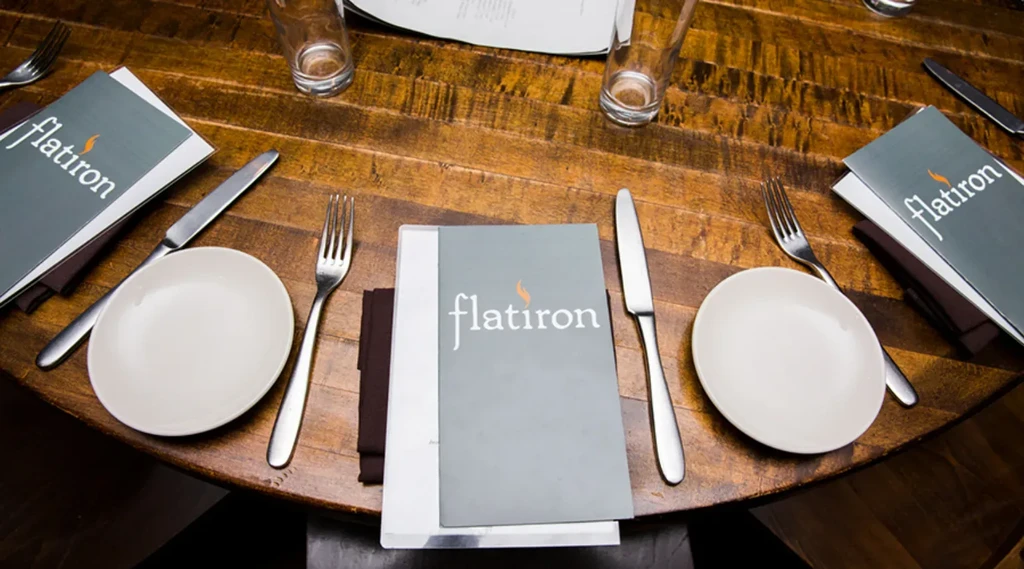 Dark wooden restaurant table set for three, with Flatiron menus.