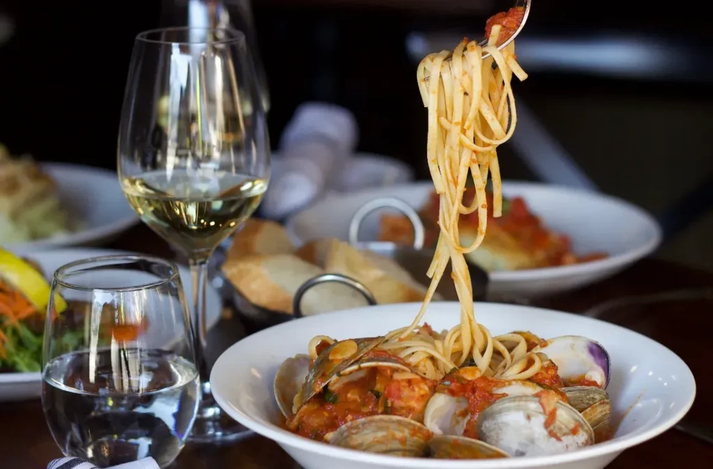 Fork lifts linguine with clams in red sauce, wine glass.