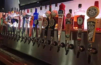 Eighteen beer taps, brand handles, and backlit liquor bottles at a bar.