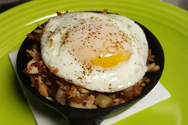 A cast iron skillet of hash topped with a fried egg.