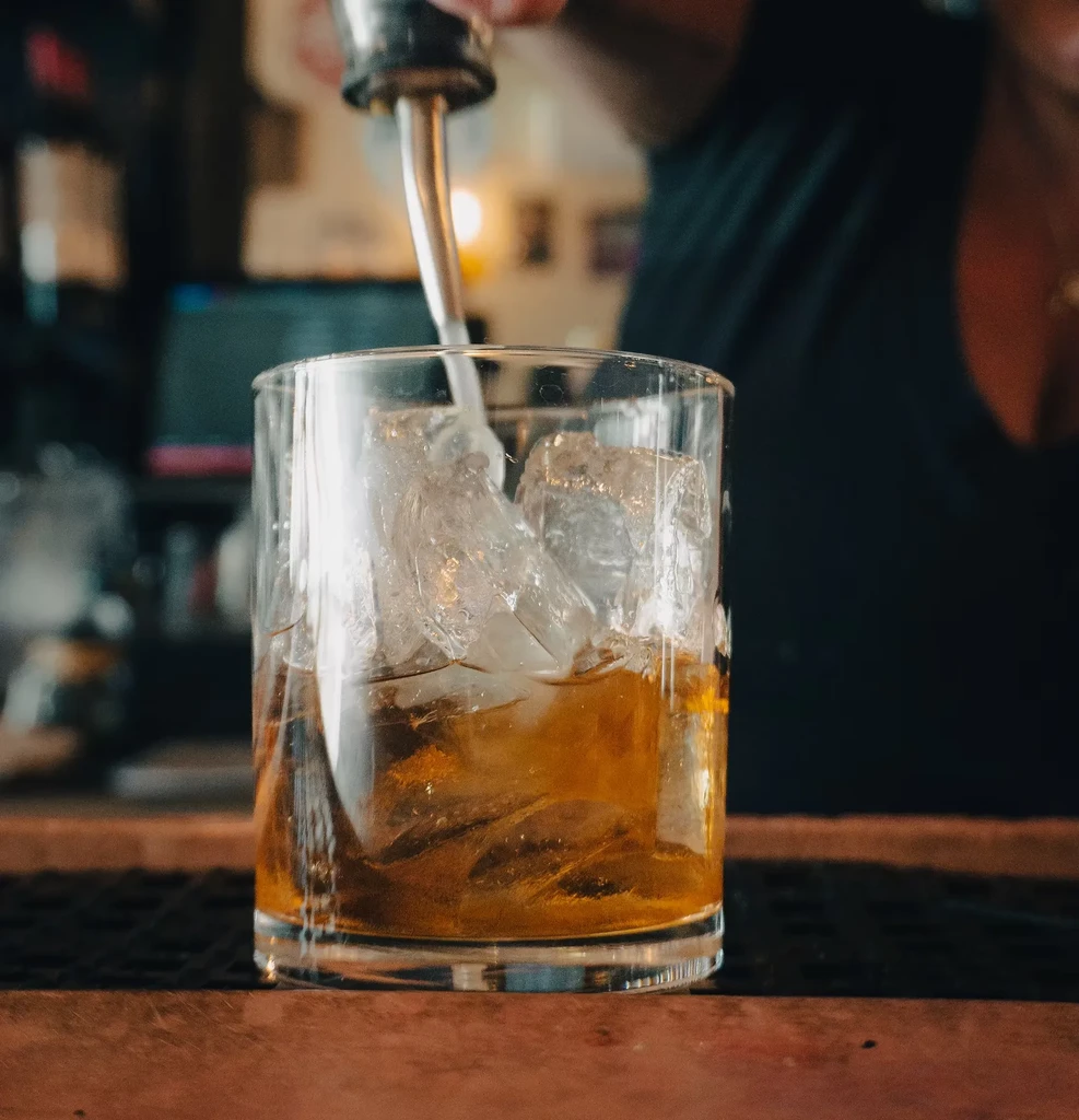 A bartender pours liquor from a spout into an ice-filled glass.