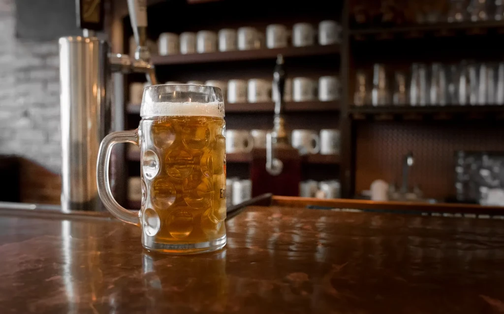 A full glass stein of beer with a foamy head on a bar.
