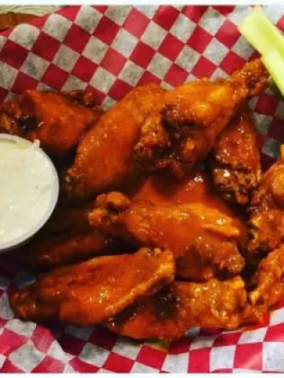 A basket of buffalo chicken wings with a side of ranch and celery.