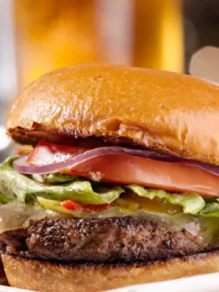 Close-up of a cheeseburger with lettuce, tomato, and red onion.