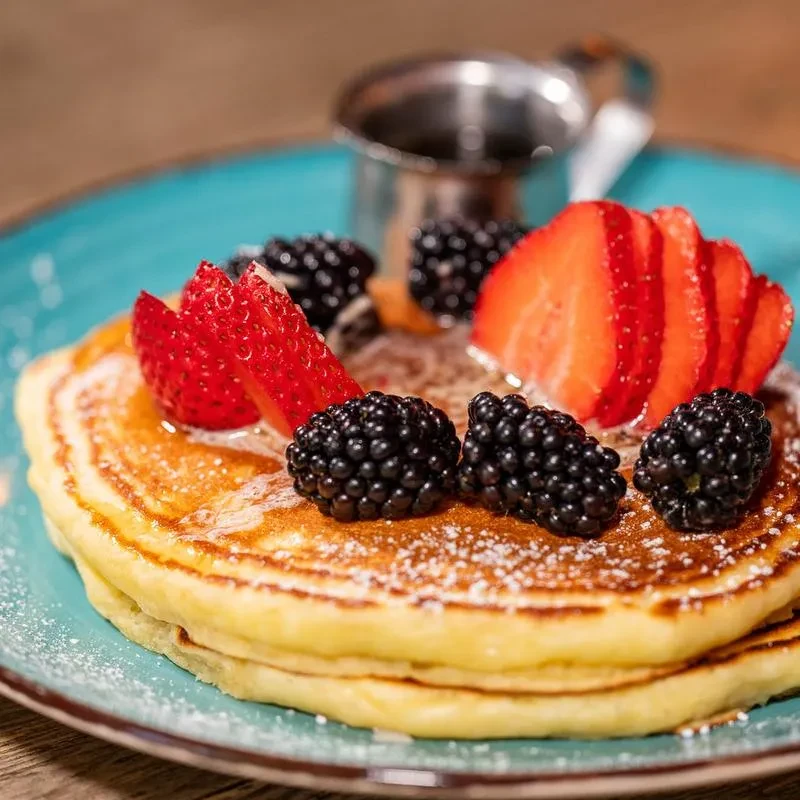 Golden-brown pancakes topped with berries and powdered sugar on a blue plate.