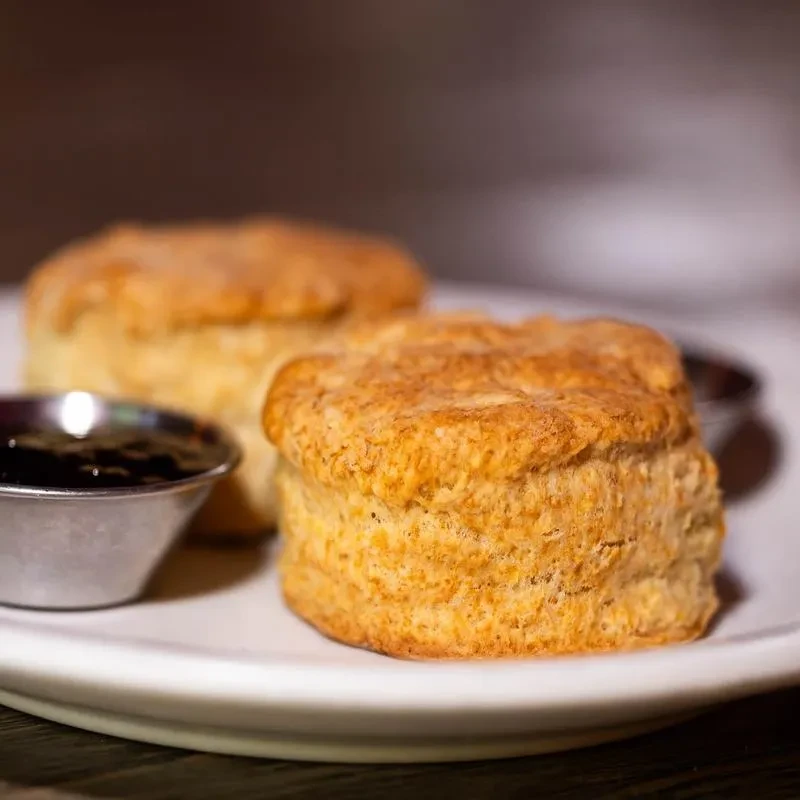 Two golden-brown biscuits with jam in a ramekin on a plate.