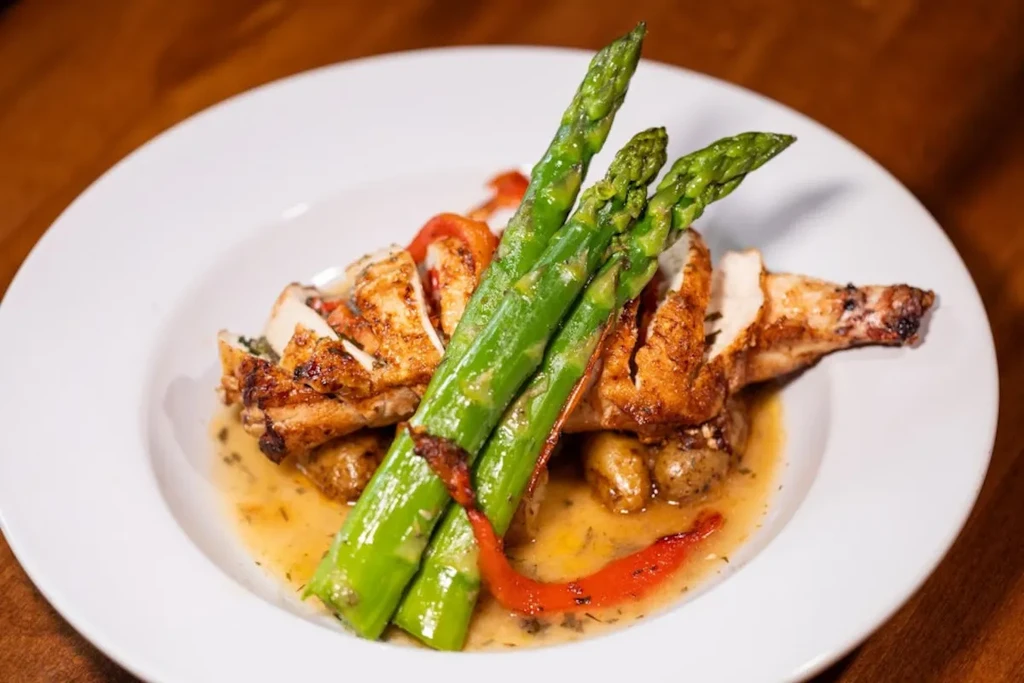 Sliced grilled chicken, tied asparagus, and potatoes with sauce on white plate.
