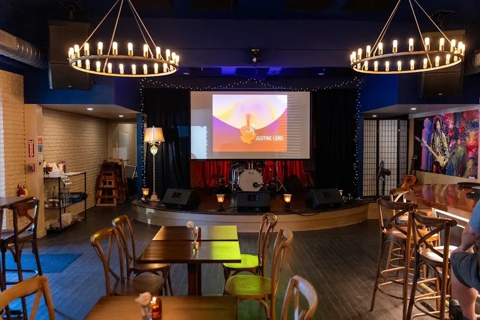 Dimly lit music venue interior with stage and 'JUSTINE LORD' screen.