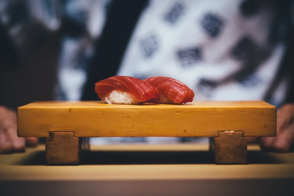 Two vibrant tuna nigiri on a wooden block at a sushi counter.