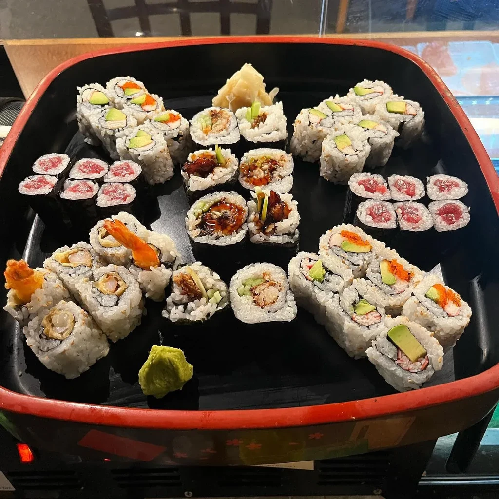 Large sushi and sashimi platter on black tray with ginger and wasabi.