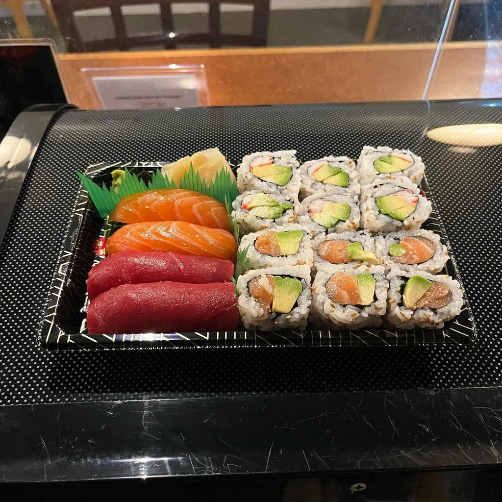 Salmon and tuna nigiri, assorted sushi rolls in a take-out container.