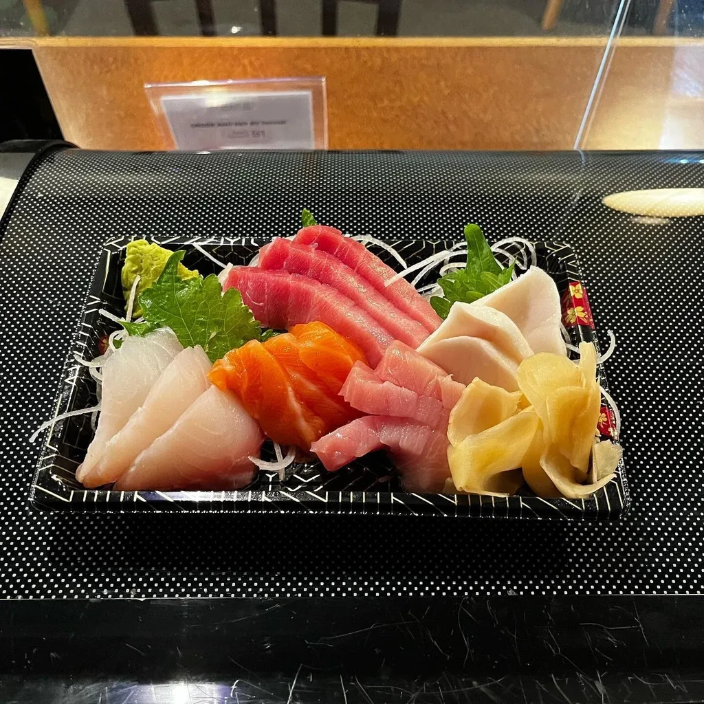 Colorful sashimi platter with raw fish and garnishes in a black tray.