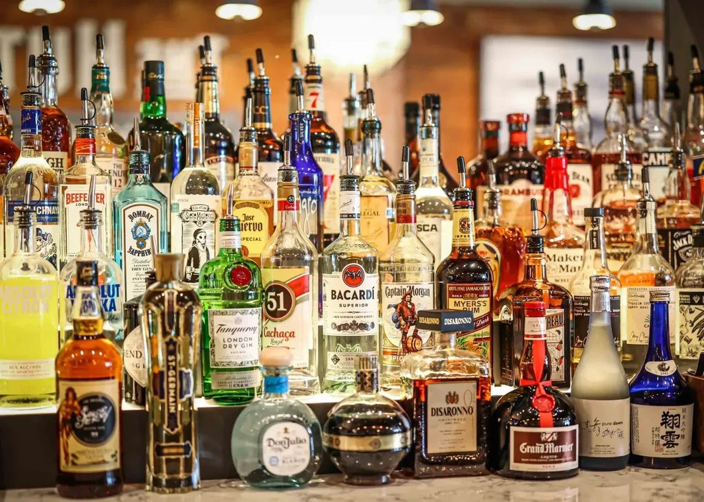 Densely packed liquor bottles with pour spouts on a well-lit bar.