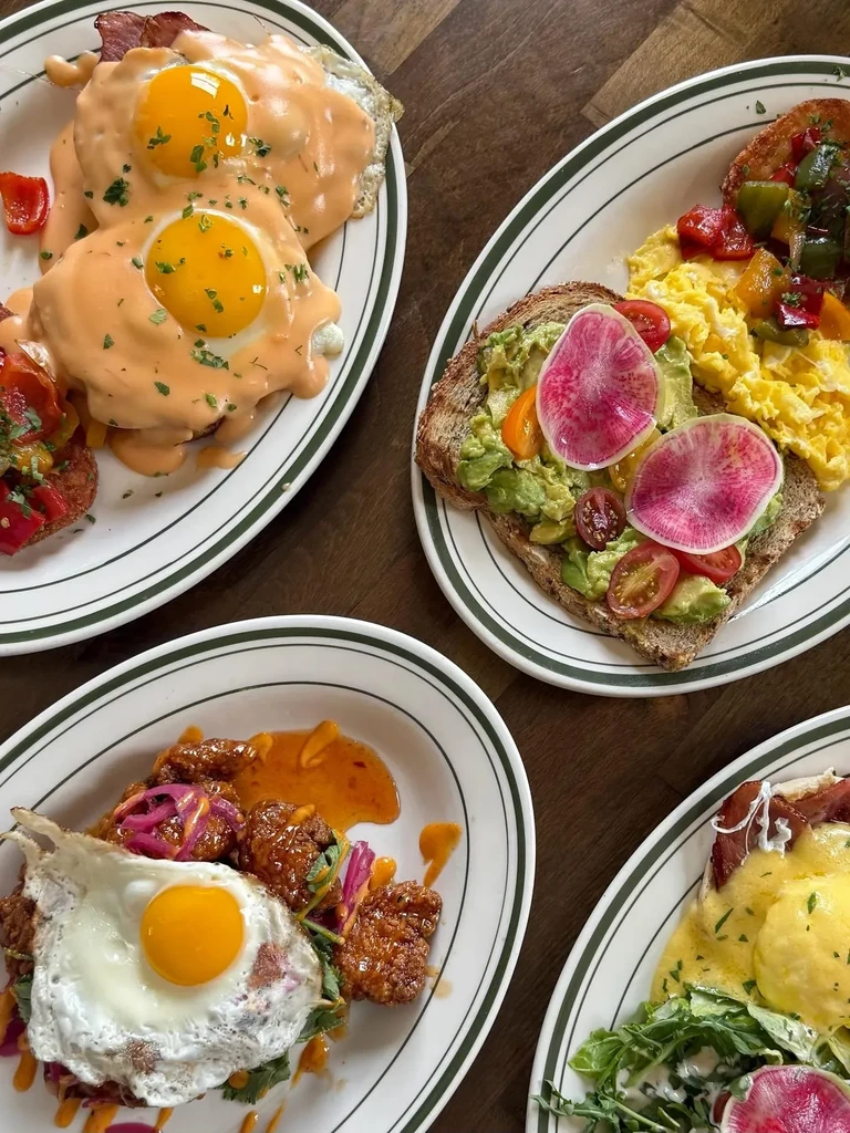 Four plates of various breakfast dishes with eggs, avocado toast, and chicken.