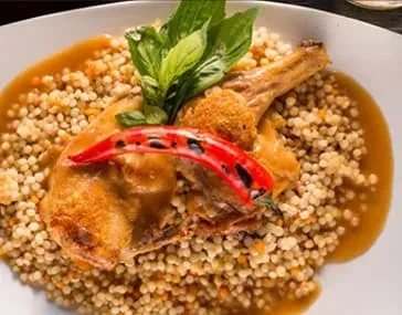 Roasted chicken thigh and couscous on a white plate with sauce.