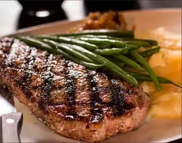 A grilled steak with green beans and mashed potatoes on a white plate.