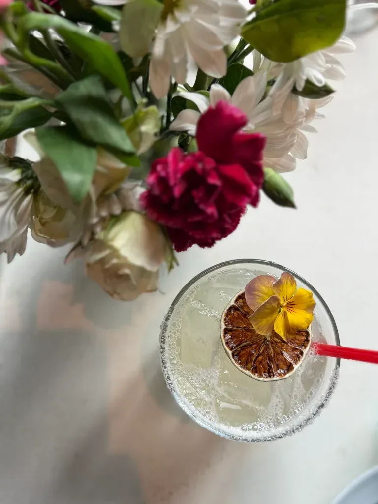 Overhead shot of a garnished cocktail and a bouquet of flowers.