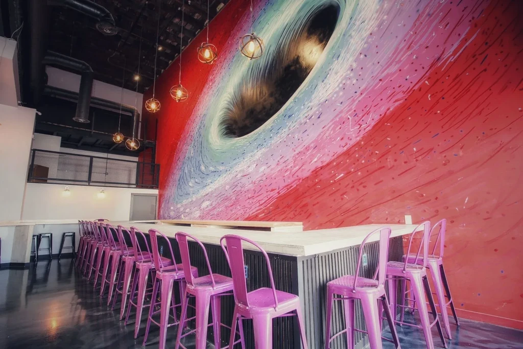 An empty bar with a black hole mural and purple barstools.