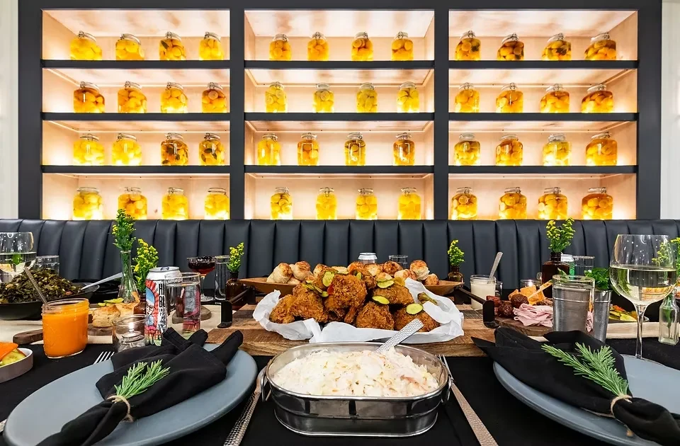 A long table set with food and drinks in front of illuminated shelves.