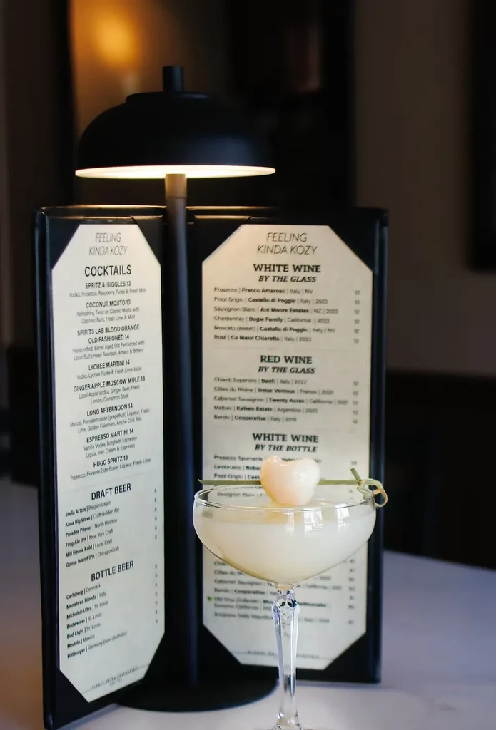 A lychee martini sits on a table next to an illuminated menu.