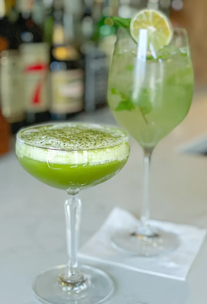 Two green cocktails, one with lime and mint, the other with foam.