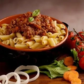 A bowl of penne pasta with bolognese sauce, basil, onions, and carrots.