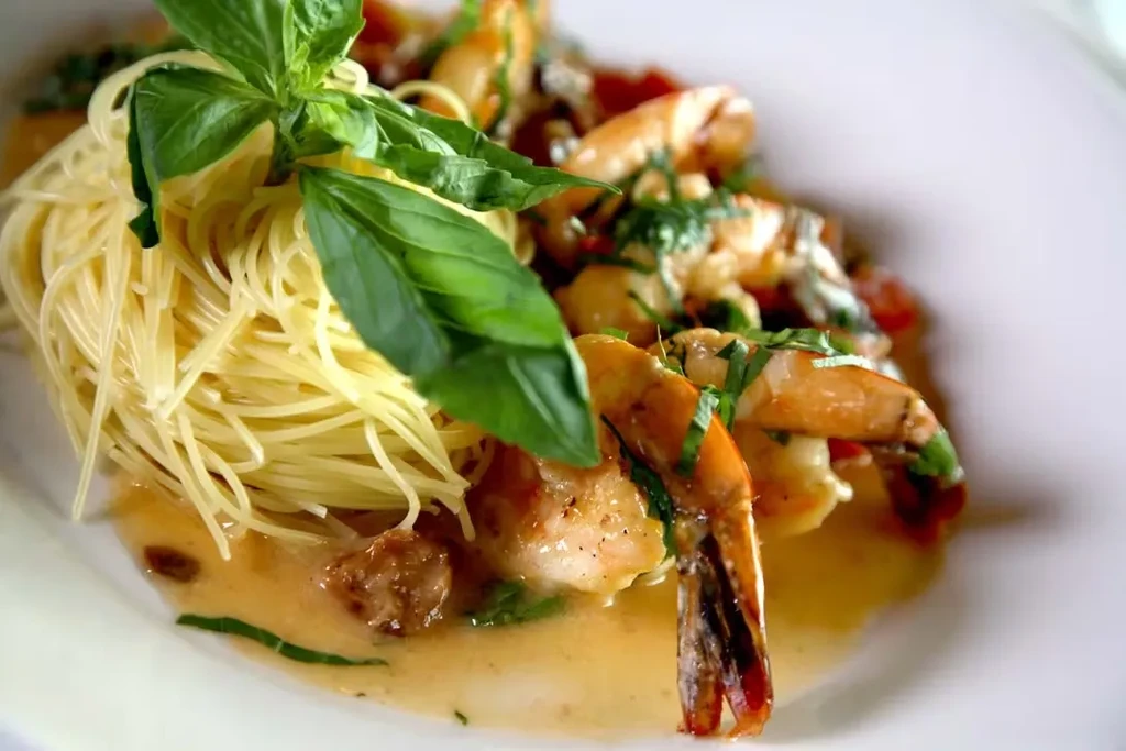 Shrimp scampi with pasta and basil on a white plate.