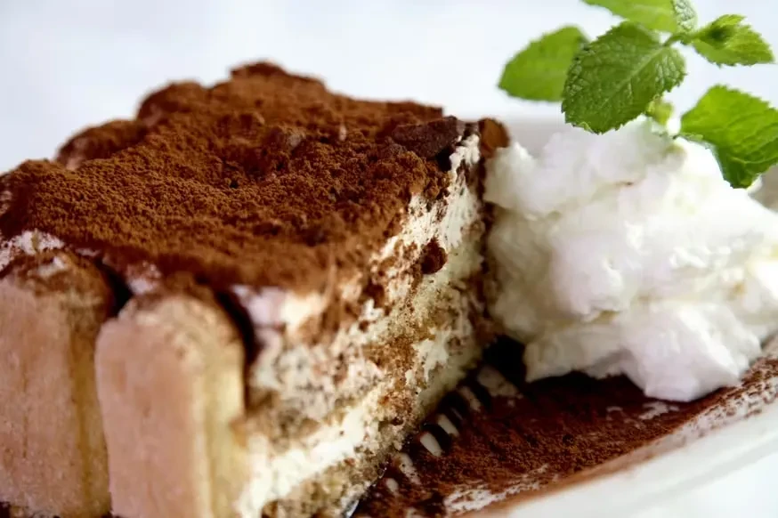 A slice of tiramisu with whipped cream and a mint sprig.