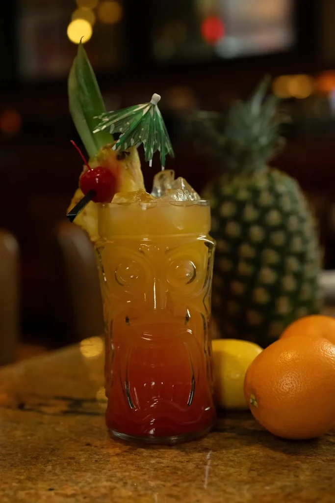 A Tiki glass with a drink, pineapple, cherry, and mini umbrella.