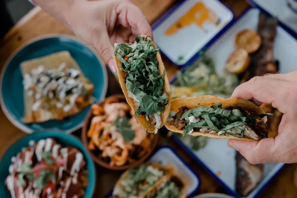 Two hands holding tacos filled with meat, lettuce, and sour cream.