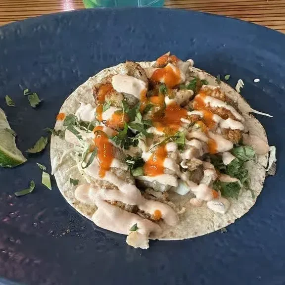 A fish taco on a blue plate, with hot sauce and crema.