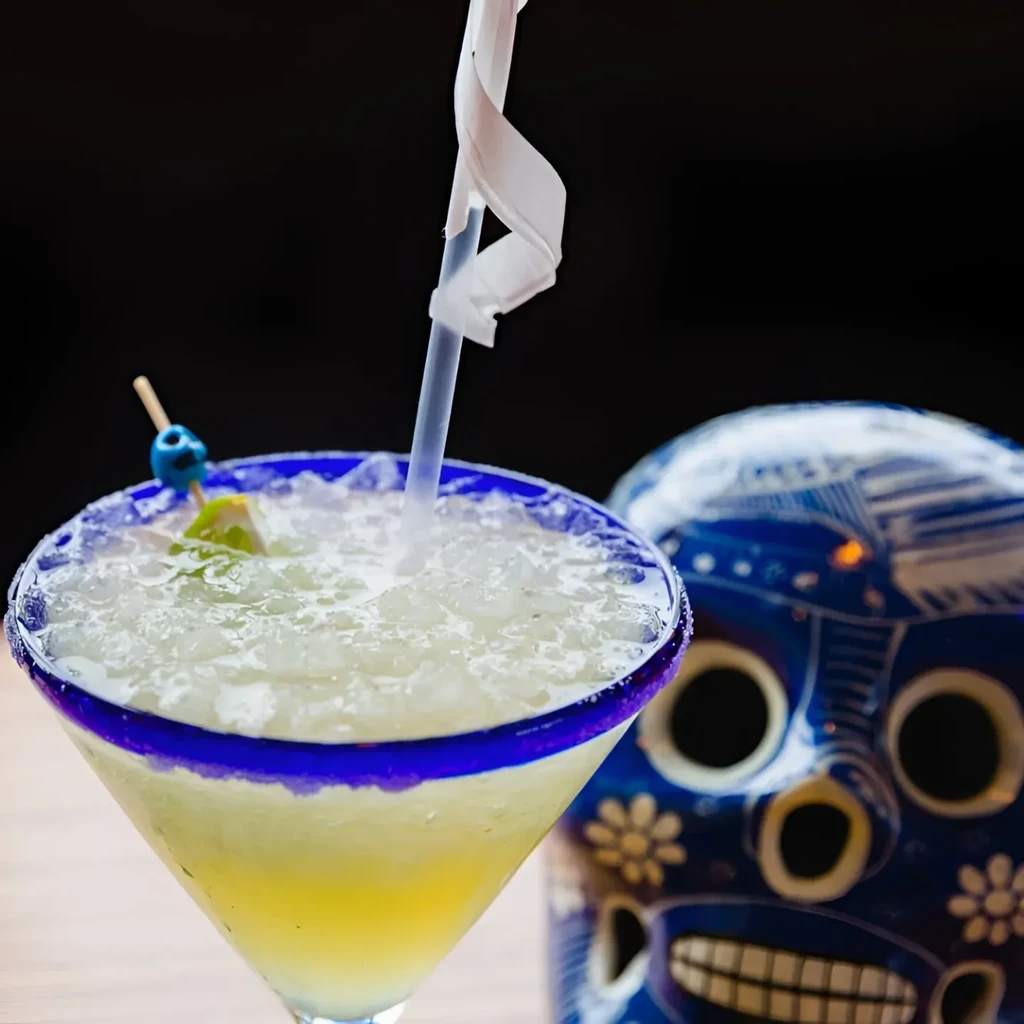 A margarita in a blue-rimmed glass next to a blue skull.