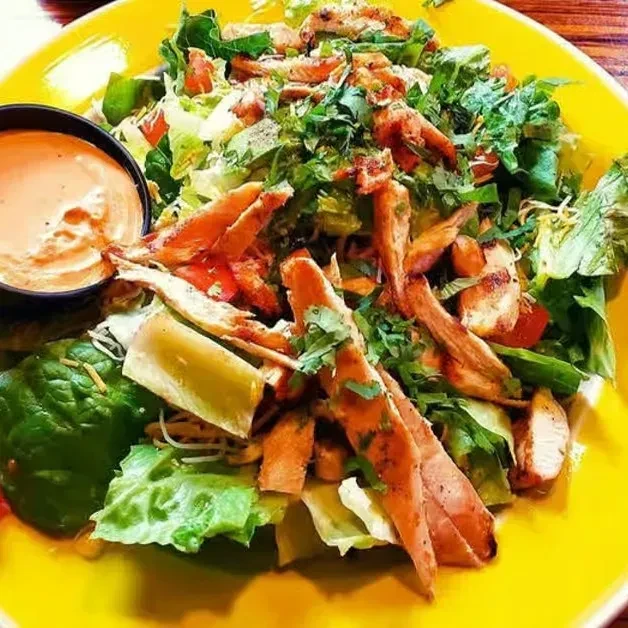 A vibrant salad with chicken, mixed greens, and dressing on a yellow plate.