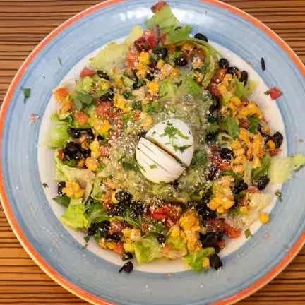 A colorful salad with corn, black beans, lettuce, and sliced egg.