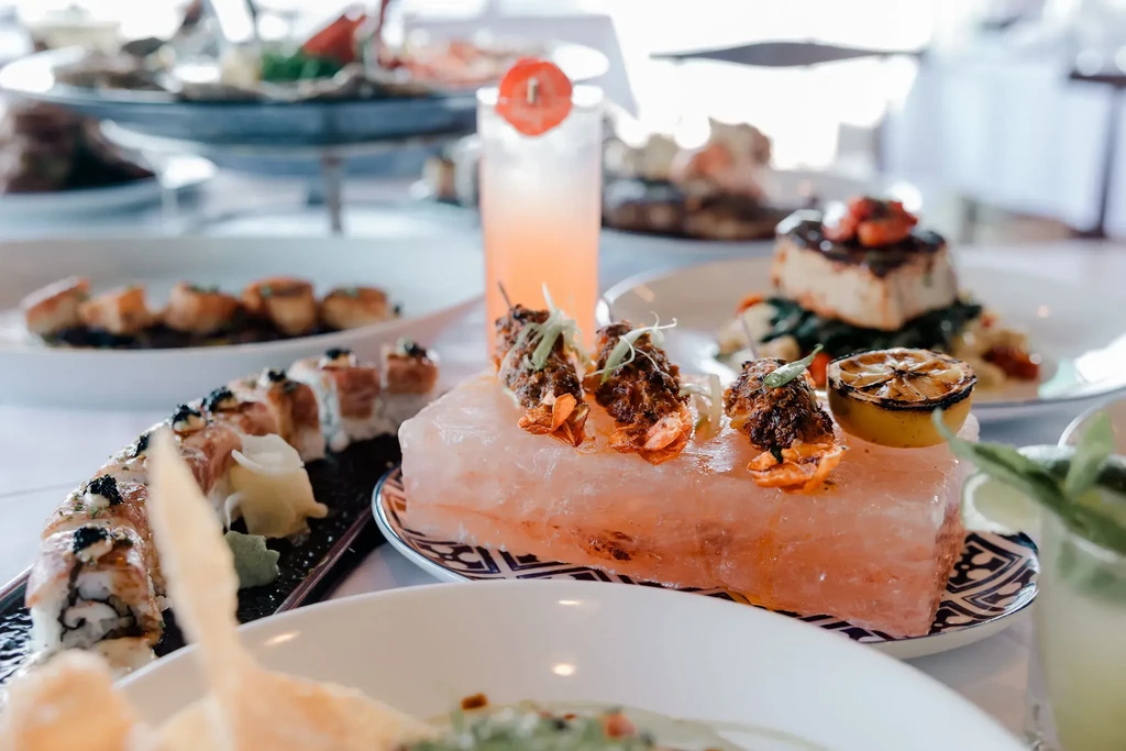 Close-up of lobster tails on a pink salt block with sushi and cocktails.