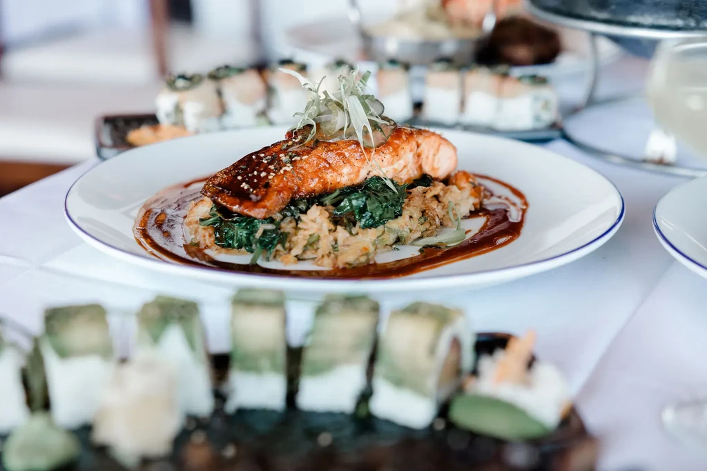 A plate of cooked salmon, greens, and rice with sushi rolls.
